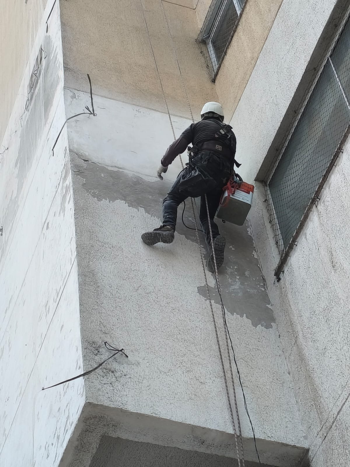 Profissional em rapel preparando a superfície da fachada