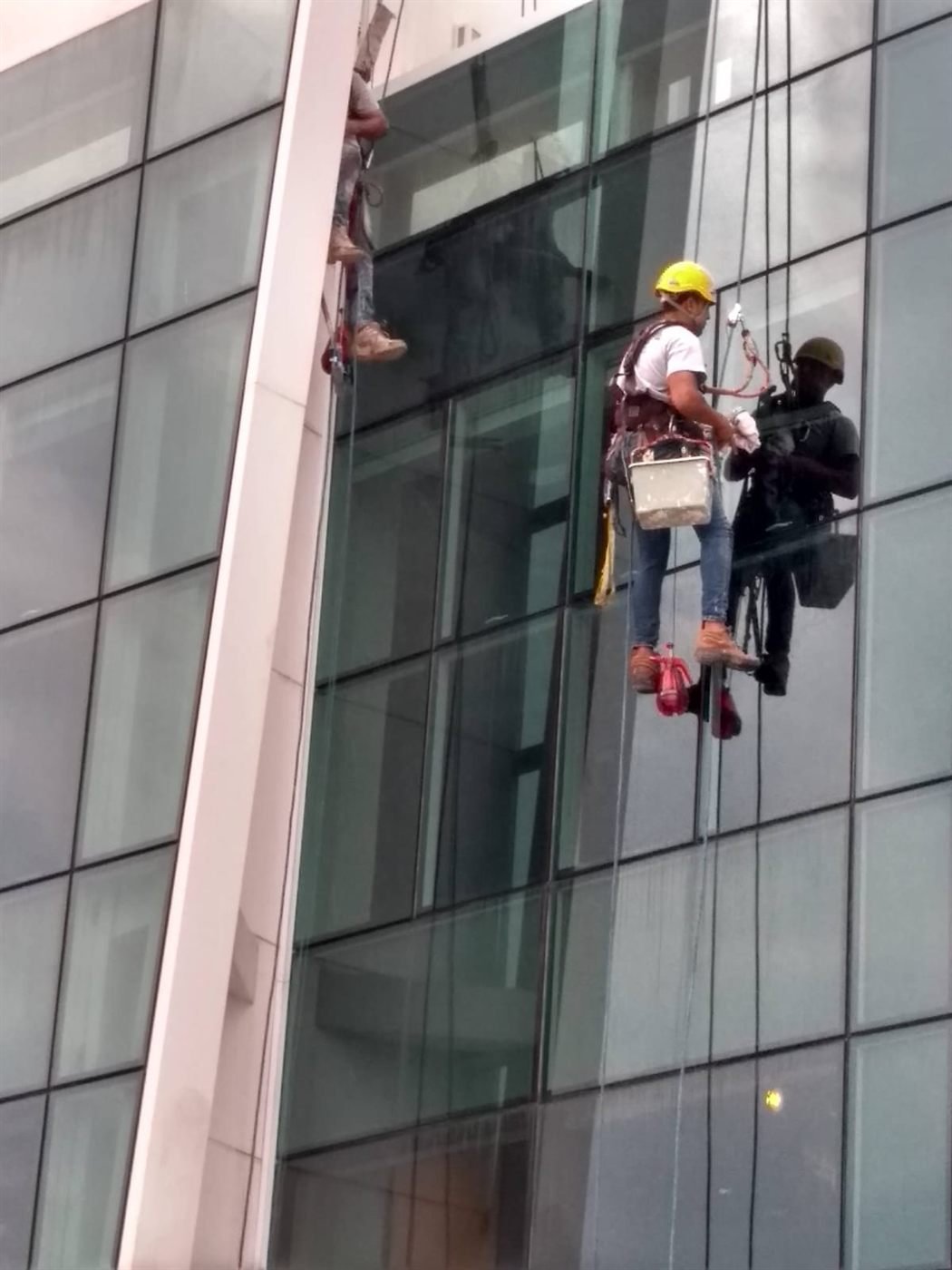 Alpinistas industriais em fachada envidraçada